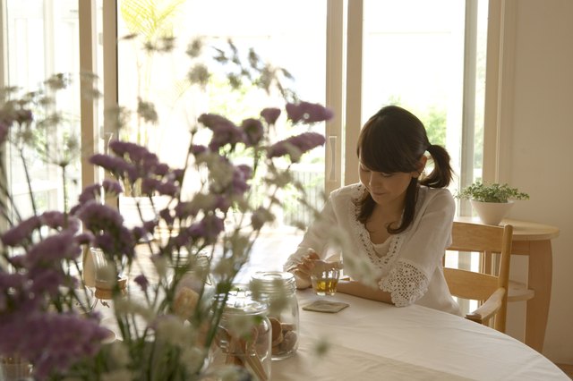 Woman with cup of tea, sitting at table in home, flowers in foreground