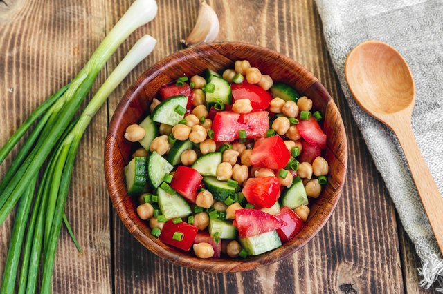 Bowl of chickpea salad with vegetables next to a wood spoon