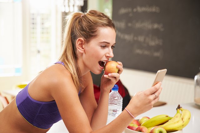 Woman in sports bra eating apple looking at her smart phone