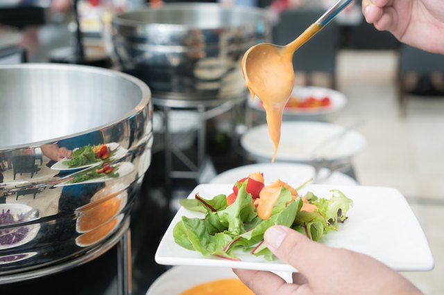 Tablespoon measure of creamy thousand island dressing being poured over fresh garden salad in breakfast buffet at hotel.